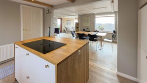 A modern kitchen with a central island, a dining area with a table and chairs, and a view through a window. - Awesome home in Knebel with house sea view (Knebel)