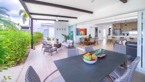 An open-plan living area with a dining table, chairs, and a kitchen in the background. - Luxury Walk-to-Beach 3BR Oasis , Playa Avellanas (Playa Avellanas)