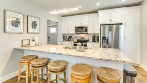 Cocina moderna con armarios blancos, electrodomésticos de acero inoxidable e isla de granito con taburetes.
