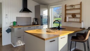 Una cucina moderna con mobili bianchi, un piano di lavoro in legno, una cappa aspirante nera e vista sull'esterno attraverso un'ampia finestra.