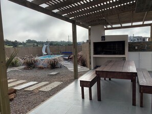A covered outdoor area with a pool, a barbecue grill, and a dining table. - Frente al mar. Piscina climatizada. Parrillero. Los mejores atardeceres. (Punta Negra)
