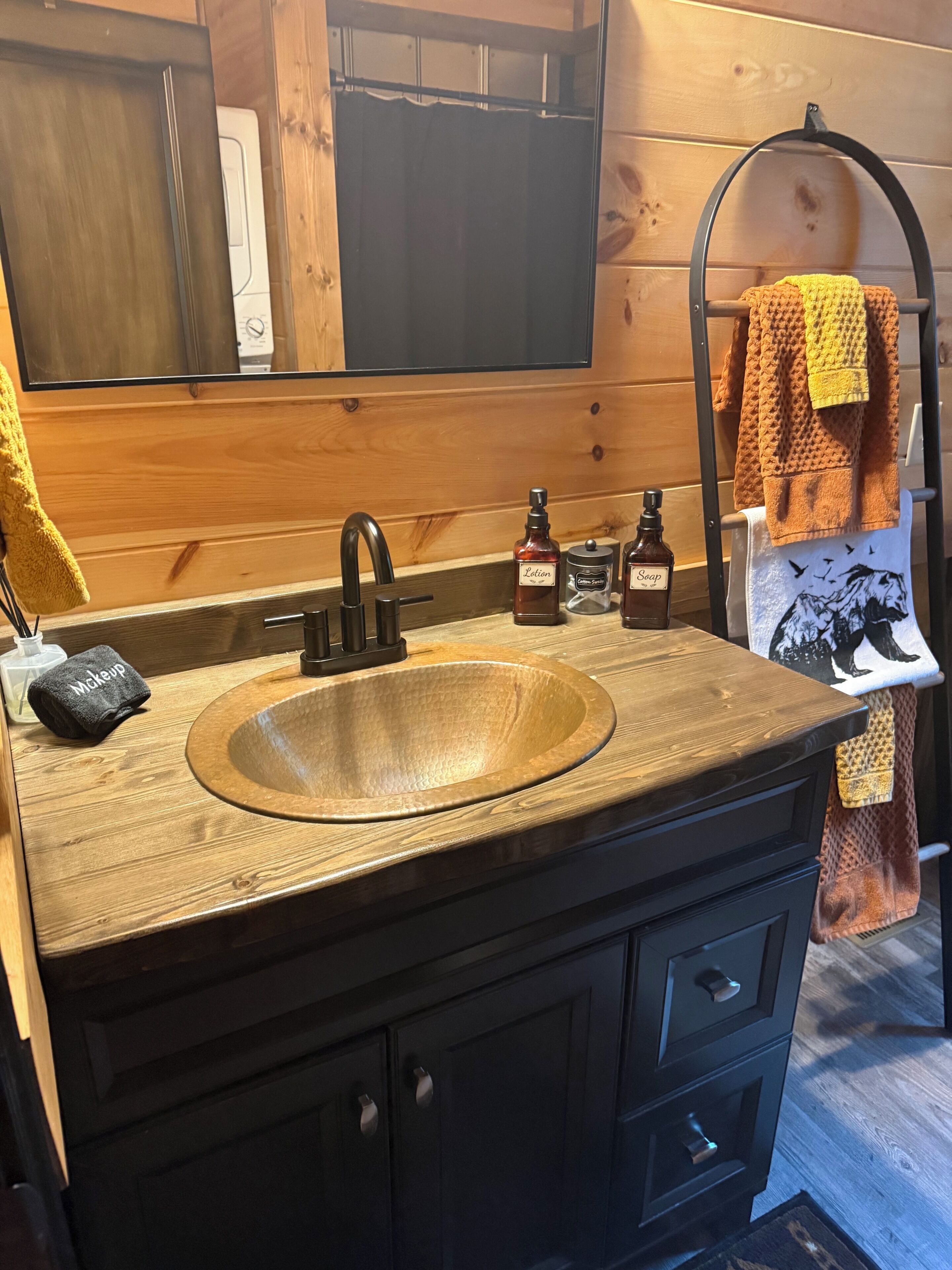 A wooden vanity with a round sink, a mirror, and a towel rack with towels.