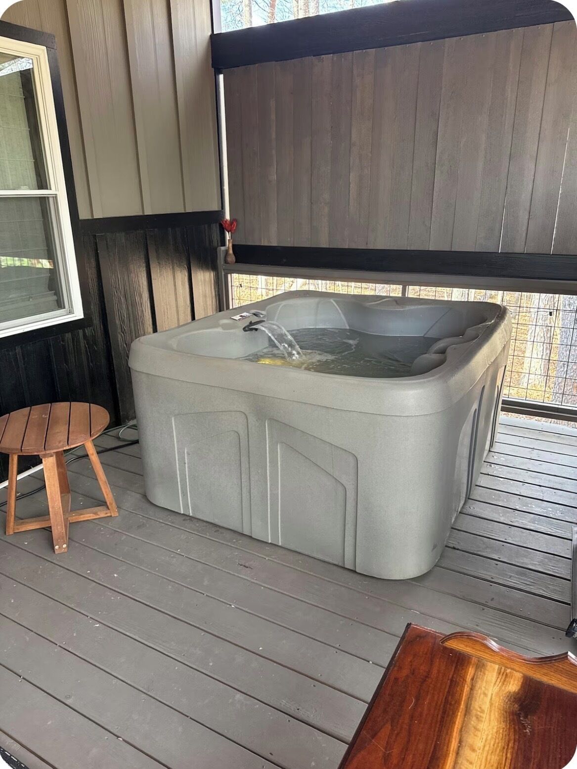 Ein Whirlpool auf einer Holzterrasse mit einem Holzstuhl und einem Tisch in der Nähe.