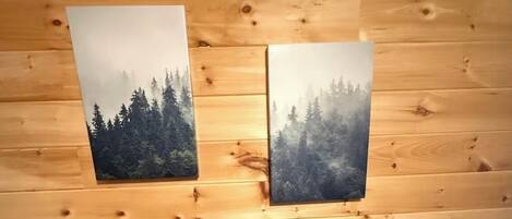 A wooden cabin interior with two framed pictures of forests on the wall, a marble toilet, and a wooden floor.