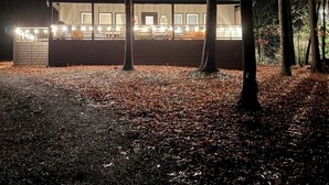 Una cabaña con terraza, rodeada de árboles y suelo cubierto de hojas.