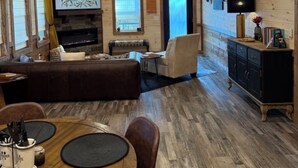 Un interior de cabaña acogedor con chimenea, pisos de madera, una zona de comedor y un ventilador de techo.
