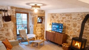 Uma sala de estar acolhedora com parede de pedra, lareira, sofá, TV e uma poltrona.