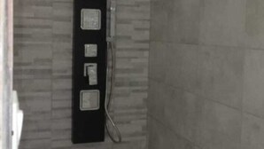 Un baño con pared de azulejos, un panel vertical negro con ducha y un enchufe a la vista.