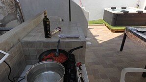Una cocina exterior con estufa a gas, olla y sartén sobre una encimera de azulejos.