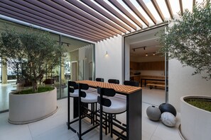 A modern kitchen with a wooden countertop and bar stools, a large potted plant, and a dining area with a glass wall. - 4BR Coastal Haven w Private Pool Al Zorah (Ajman)