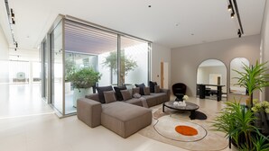 A modern living room with a sectional sofa, a coffee table, and a glass door leading to a balcony. - 4BR Coastal Haven w Private Pool Al Zorah (Ajman)