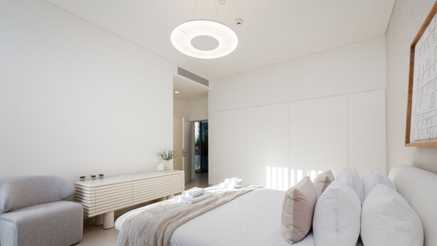 A modern bedroom with a bed, bedside tables, a bench, and a circular light fixture. - 4BR Coastal Haven w Private Pool Al Zorah (Ajman)