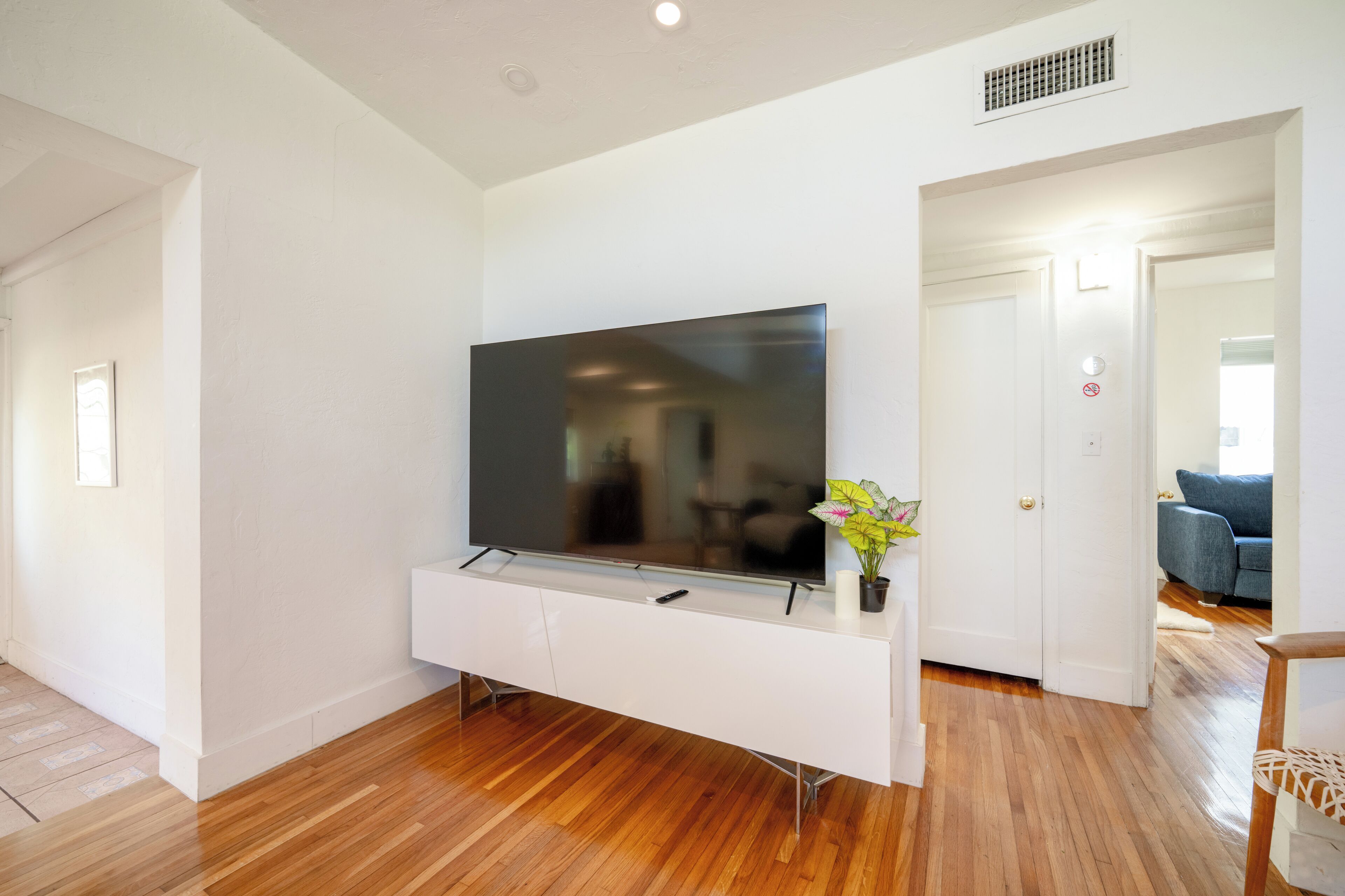 Een moderne woonkamer met een flatscreen televisie bevestigd aan een witte console, houten vloeren en een deur die naar een andere kamer leidt.