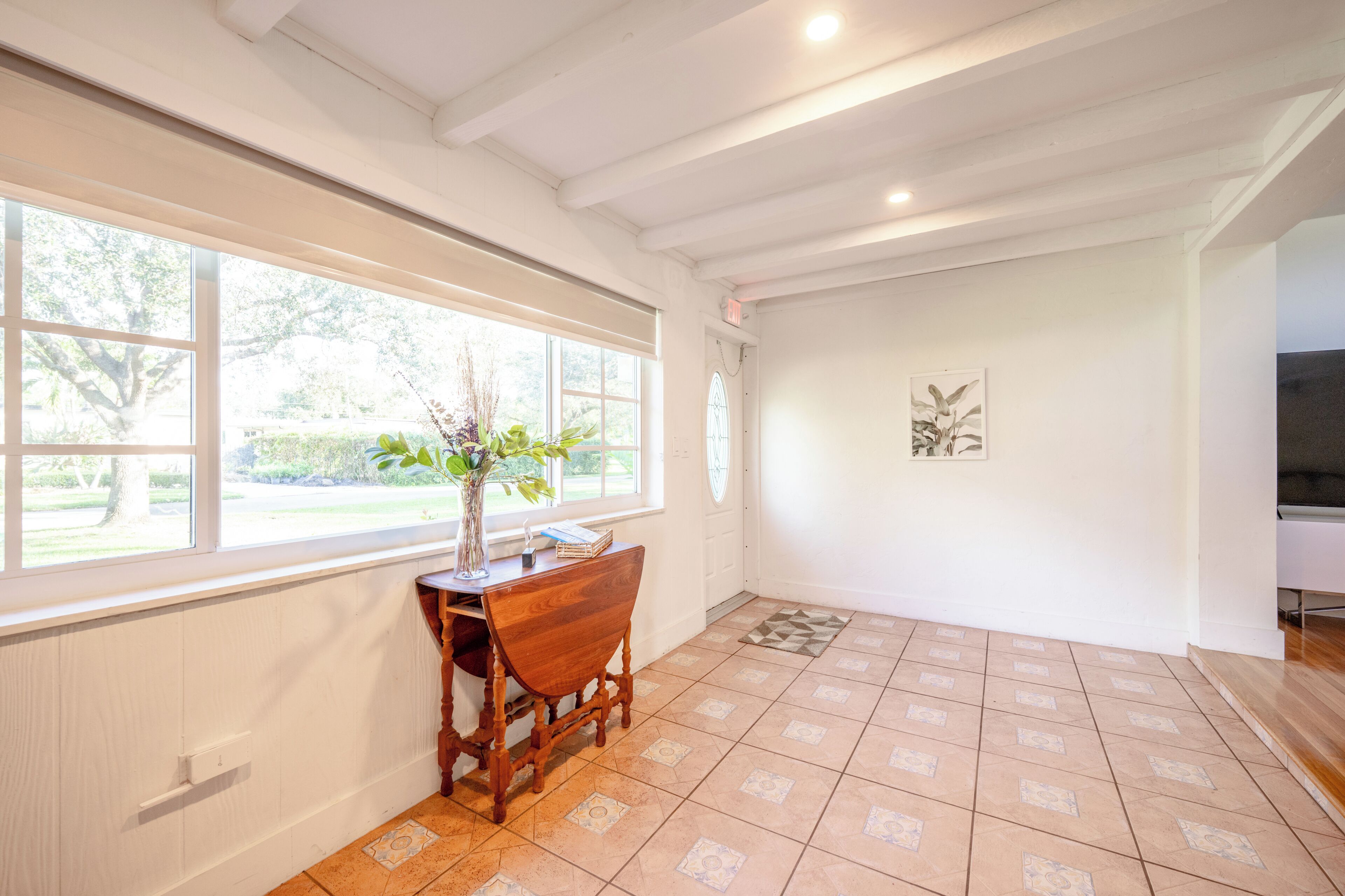 A room with a large window, wooden furniture, and a tiled floor.