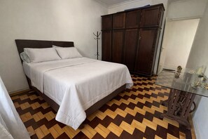 A bedroom with a bed, a wardrobe, and a glass table with decorative items.