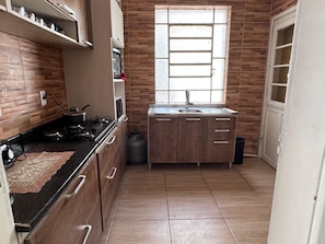 A kitchen with a gas stove, a sink, and wooden cabinets. - Apto Pet Friendly com Ar condicionado no Centro (Bagé)