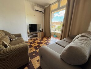 A living room with a patterned floor, two sofas, a TV, and a balcony with a view.