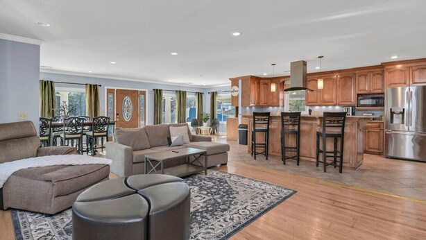 A spacious living room with a sofa, ottoman, and a coffee table, a dining area with chairs, and a kitchen with wooden cabinets and a stainless steel refrigerator. - Pond View Retreat | Bright & Spacious 3BR (West Columbia)