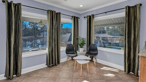 A room with a view of a lake, two chairs, a small table, and a potted plant. - Pond View Retreat | Bright & Spacious 3BR (West Columbia)