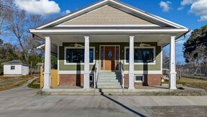 A two-story house with a front porch, a small attached garage, and a brick foundation. - Pond View Retreat | Bright & Spacious 3BR (West Columbia)