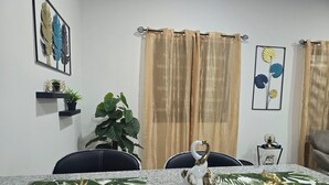Un comedor con una mesa de granito, dos sillas, una planta en maceta y un estante montado en la pared con adornos.