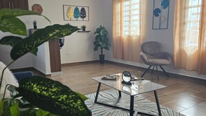 Un salón con diseño moderno, que incluye una mesa de centro de vidrio, un sillón cómodo y una planta grande en maceta.