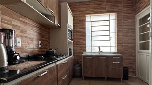 Une cuisine avec des meubles en bois, un plan de travail noir et une fenêtre avec des stores.