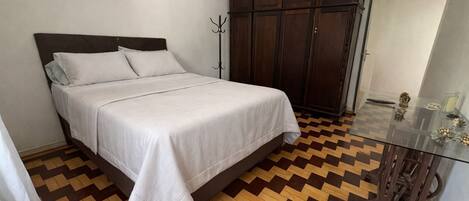 A bedroom with a bed, a wardrobe, and a glass table with decorative items.