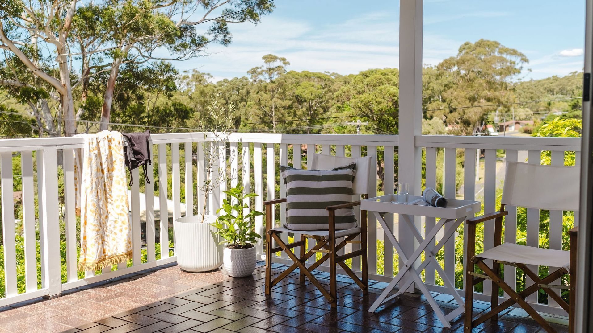 A covered outdoor area with a wooden deck, two chairs, a small table, and potted plants.