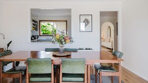 Een eethoek met een houten tafel, groene beklede stoelen en een vaas met bloemen.