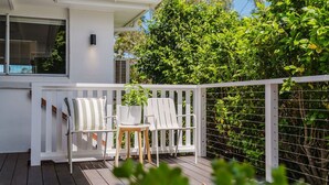 Een terras met twee witte stoelen en een klein tafeltje, omgeven door een witte hek en weelderige begroeiing.