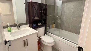A bathroom with a white sink, dark wooden cabinets, a toilet, and a glass-enclosed shower. - Quiet 2-Bedroom Garden Suite (Surrey)