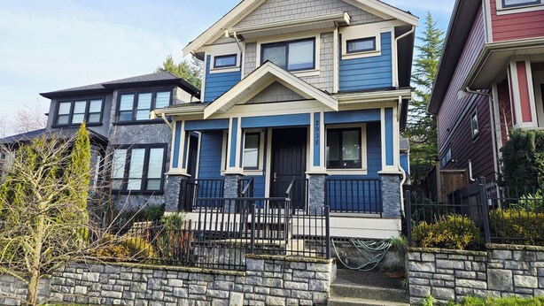 A two-story house with a stone foundation, a front porch, and a black metal fence. - Quiet 2-Bedroom Garden Suite (Surrey)