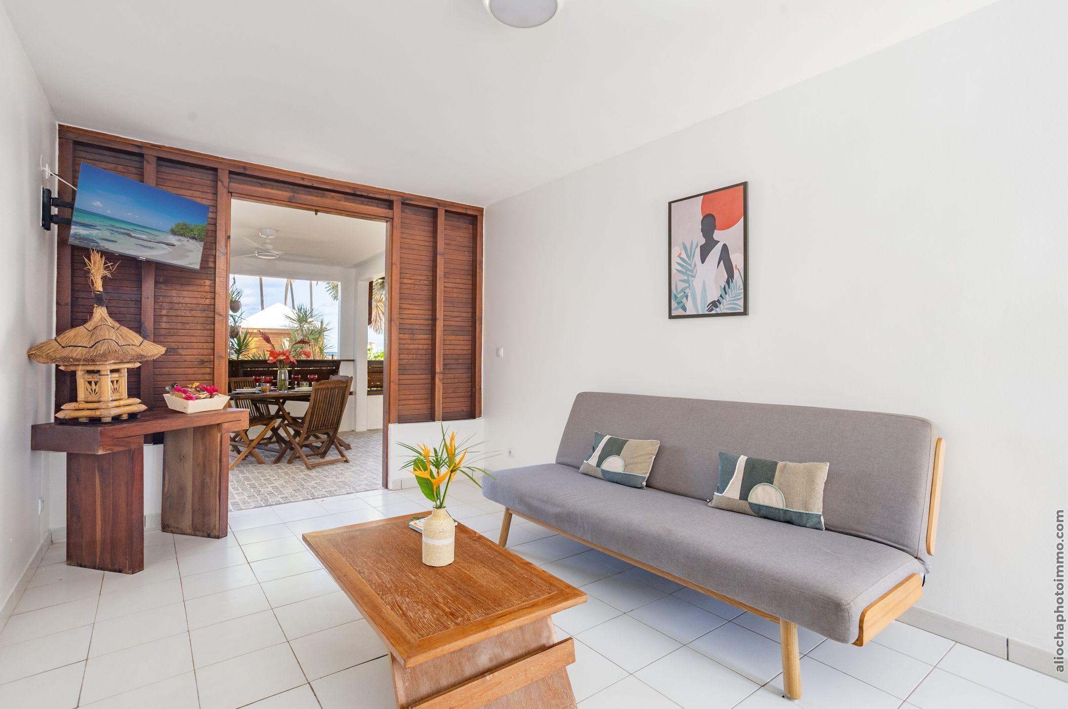 A modern living room with a grey sofa, wooden coffee table, and a dining area with a wooden table and chairs.