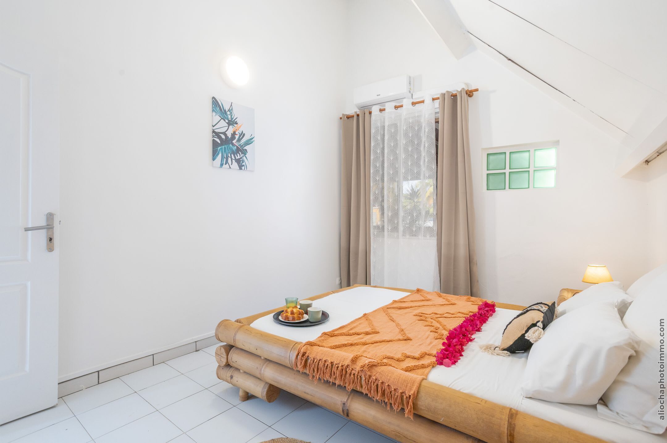 A bedroom with a bed, a window, a door, and a wall-mounted air conditioner.