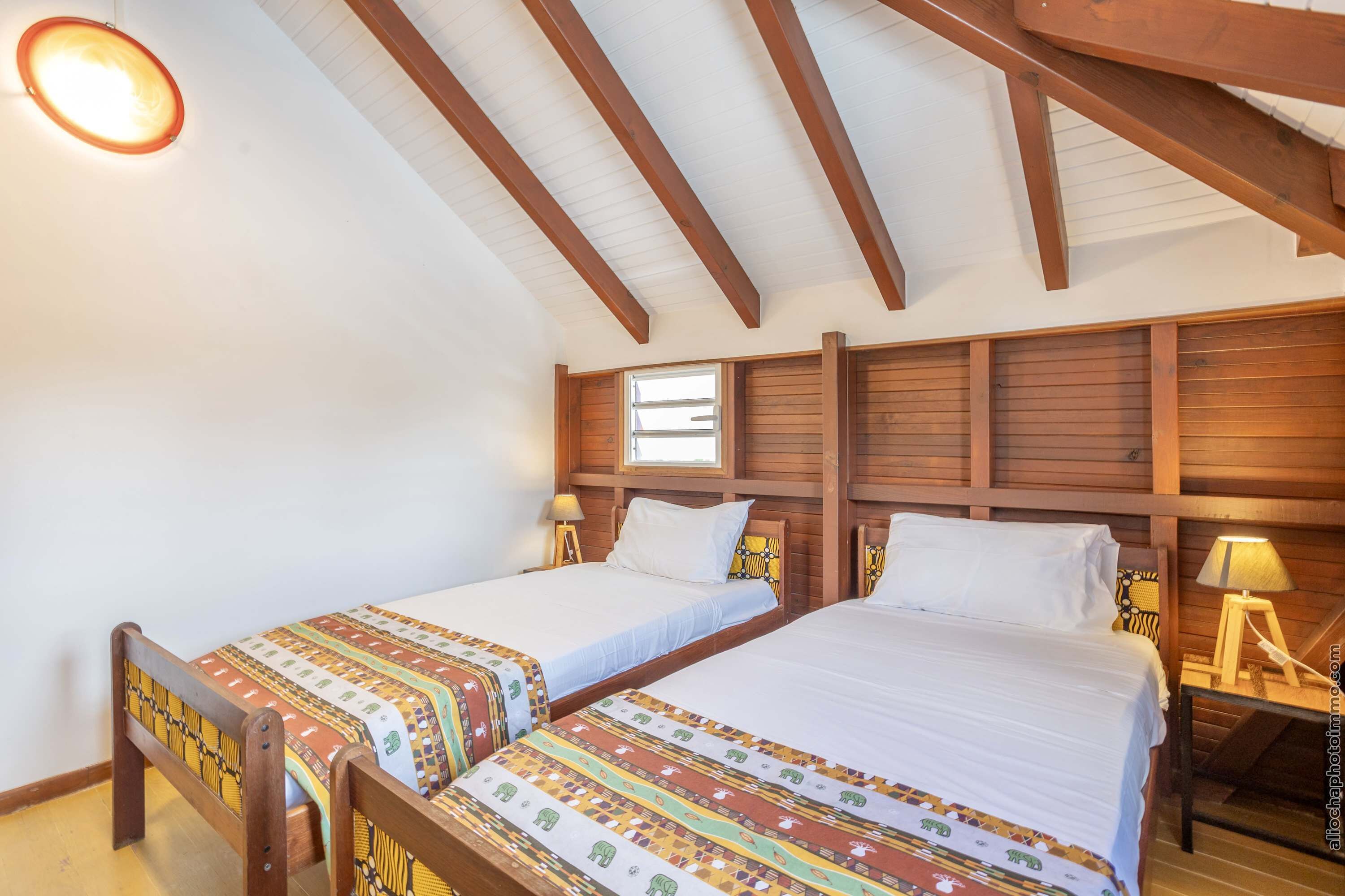 A room with two beds, wooden headboards, a window, and a ceiling with exposed beams.