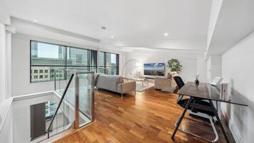A modern apartment with a spacious living area, a glass dining table, and a view of the city through large windows.