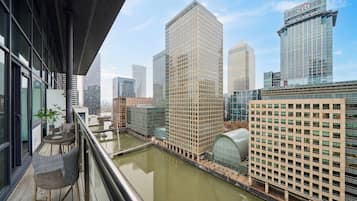 A high-rise building with a glass facade, a river in the foreground, and a balcony with outdoor furniture.