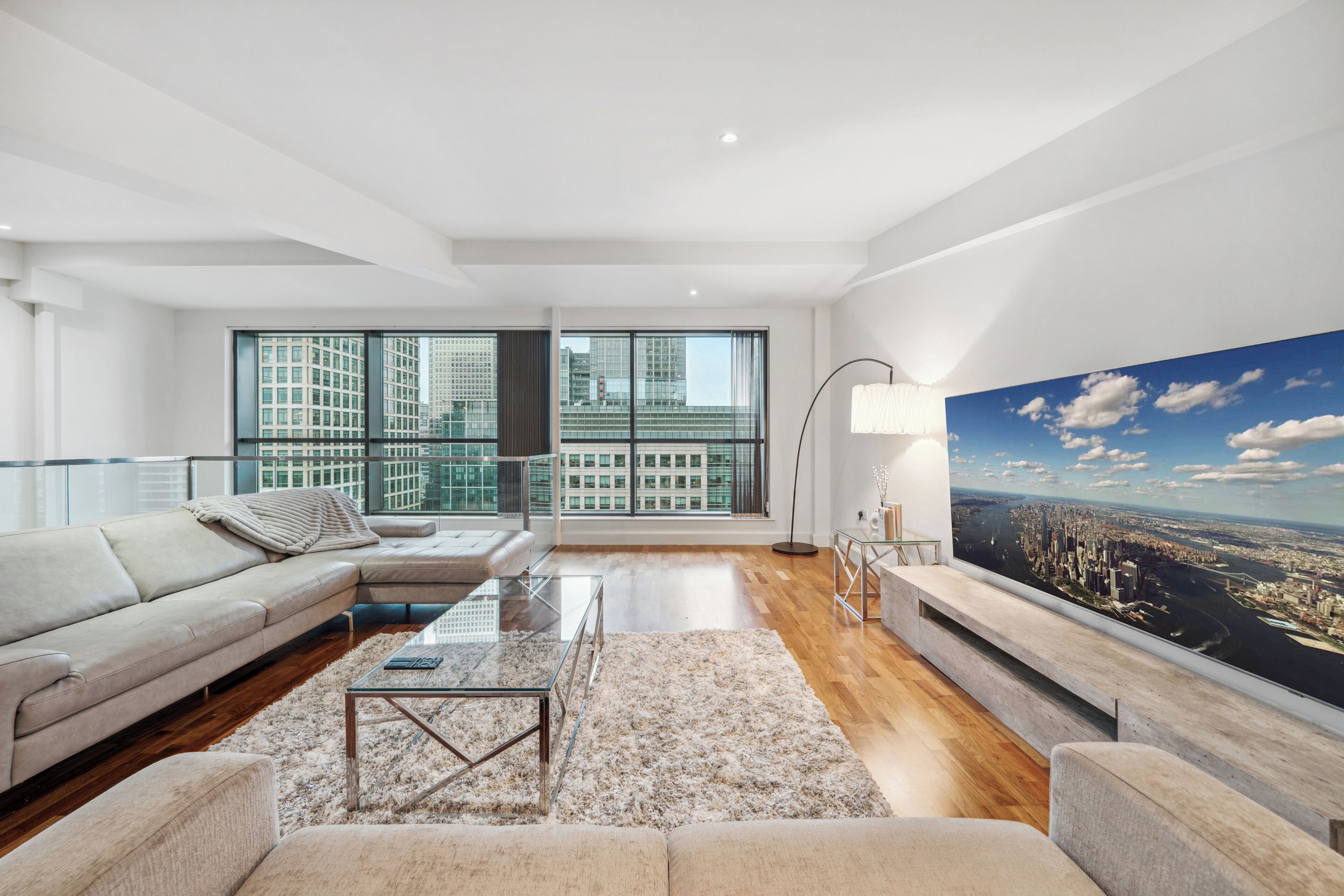 A modern living room with a large window, a sofa, a coffee table, and a painting of a cityscape.