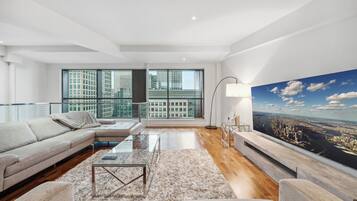 A modern living room with a large window, a sofa, a coffee table, and a painting of a cityscape.