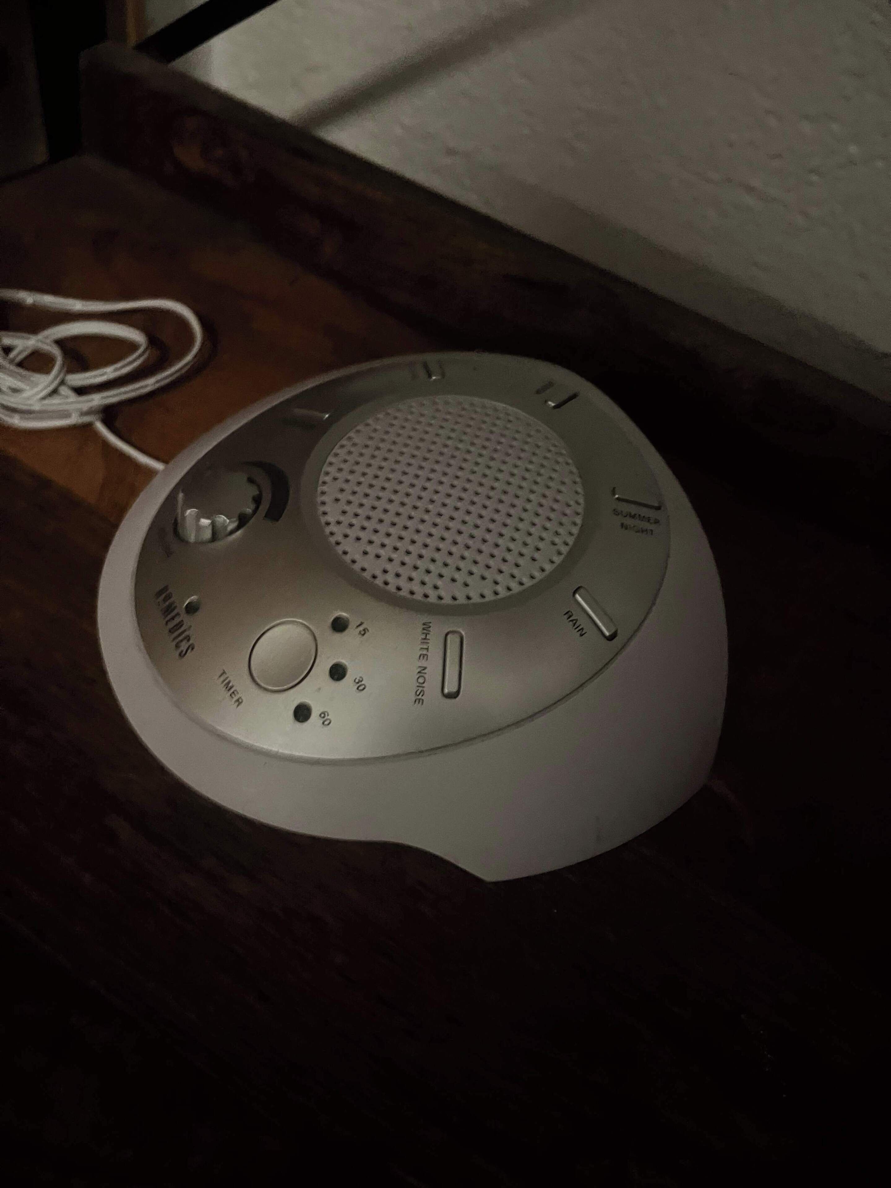 A white, circular, portable speaker with a mesh top, control buttons, and a power cord.