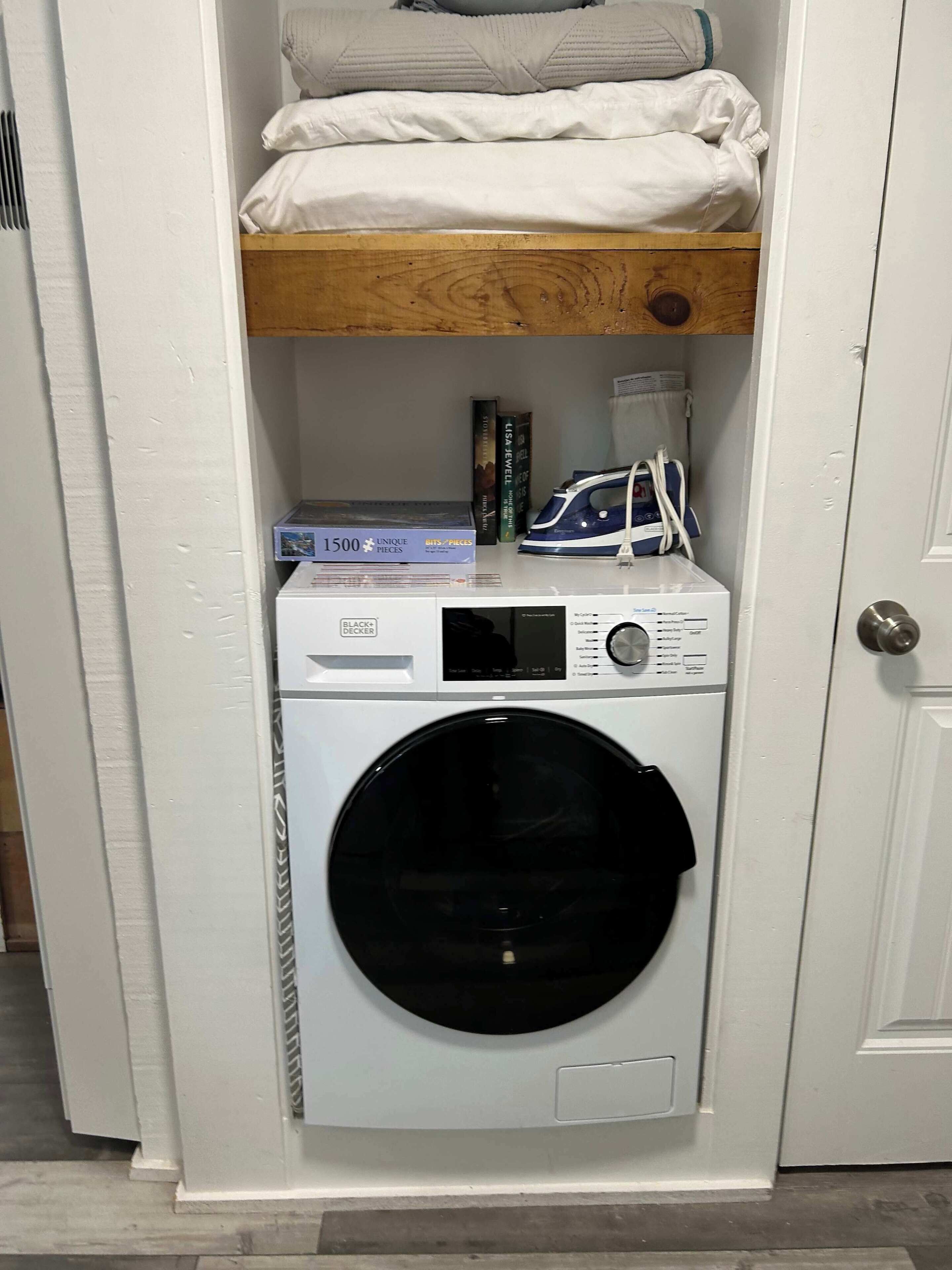Une petite buanderie comprenant un lave-linge, un sèche-linge et une étagère avec des livres et un fer à repasser.