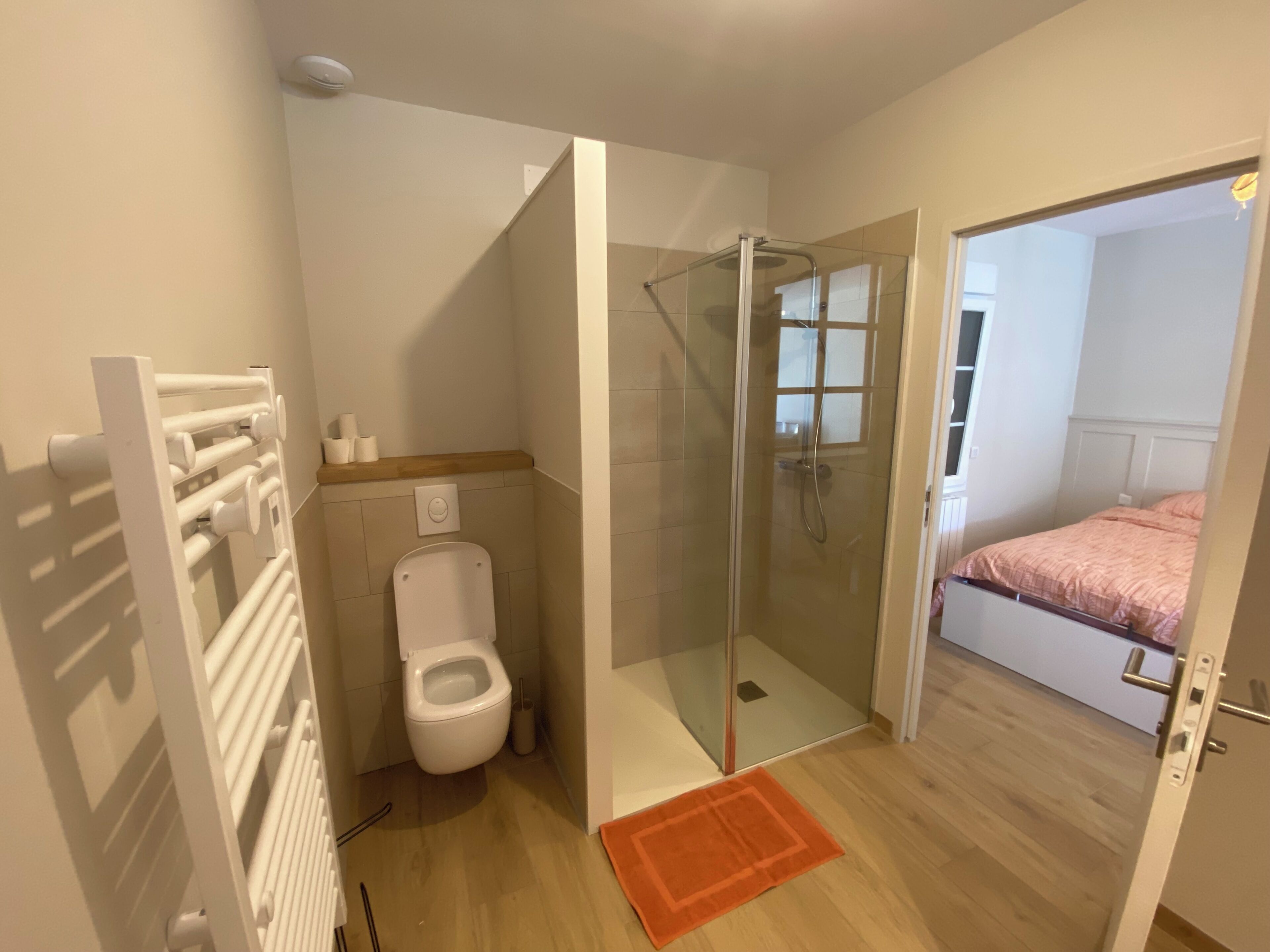 Une salle de bain avec une douche à parois de verre, des toilettes et un plancher en bois.
