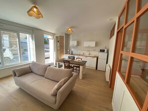 A compact living space with a sofa, dining table, kitchen area, and large windows. - Apartment T2 downtown Falaise (Falaise)