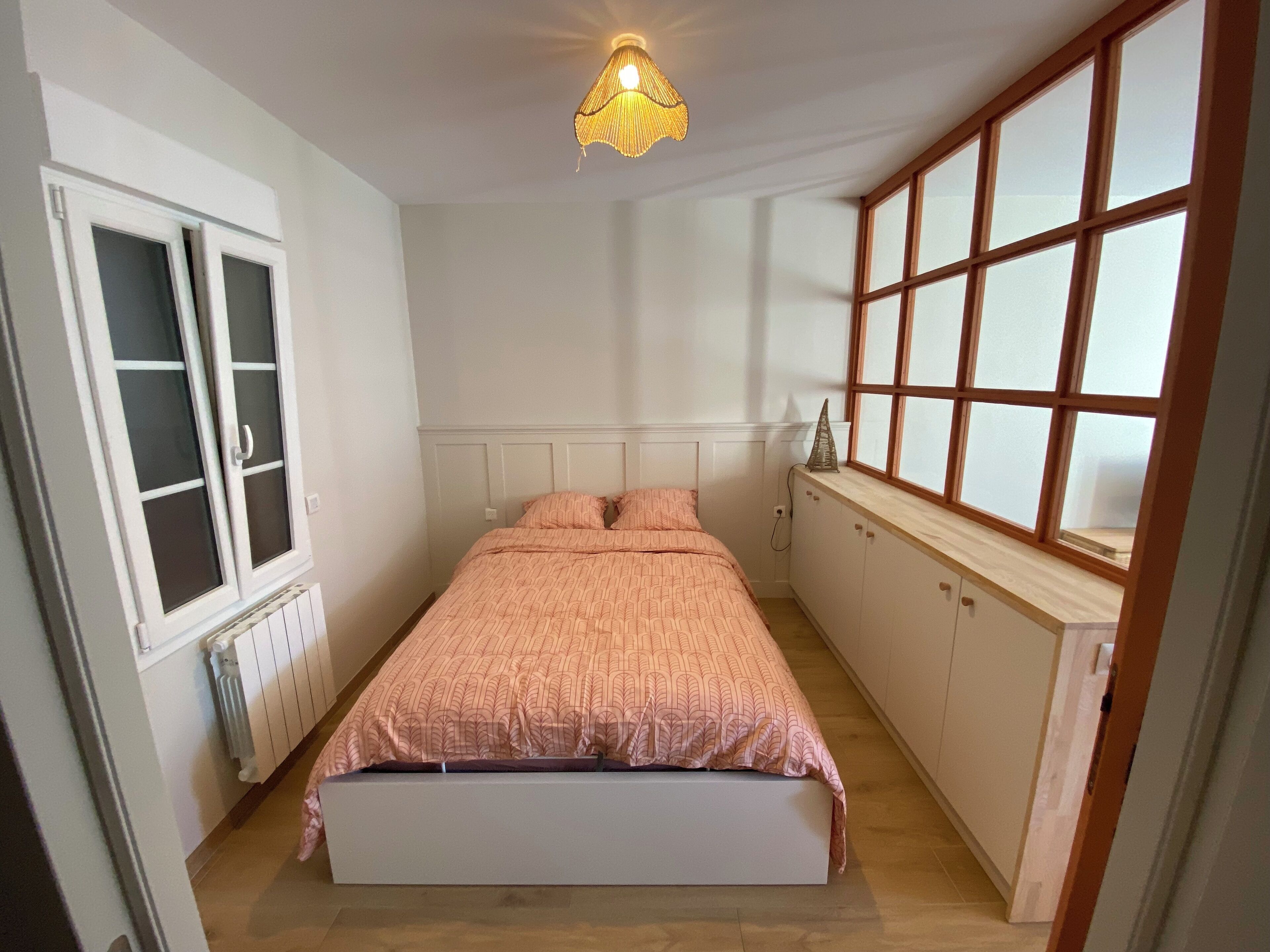Un dormitorio con cama, ventana, radiador e iluminación en el techo.