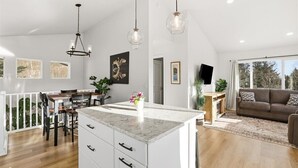 A spacious living area with a large island, dining table, and seating arrangement. - Charming 3-bedroom house in Homer perfect for your getaway (Homer)