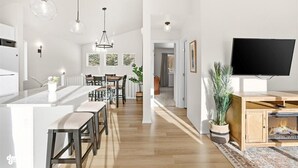 A modern kitchen with a central island, wooden dining table, and pendant lighting. - Charming 3-bedroom house in Homer perfect for your getaway (Homer)