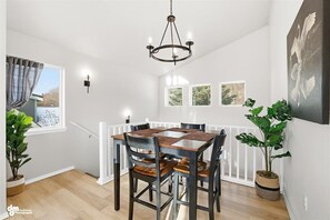 A dining area with a wooden table and chairs, a chandelier, and framed pictures on the wall.