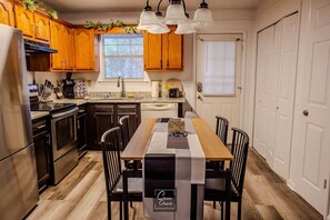 Una cocina con armarios de madera, un refrigerador de acero inoxidable, una mesa de comedor con sillas y una ventana con persianas.