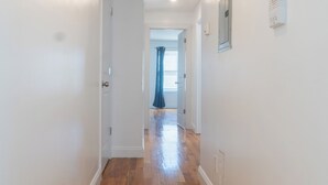 Un pasillo con piso de madera, paredes blancas y una puerta que da a otra habitación.